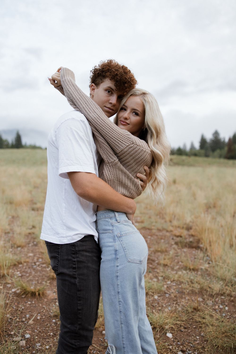 Casual couple embracing in an outdoor field with overcast sky.