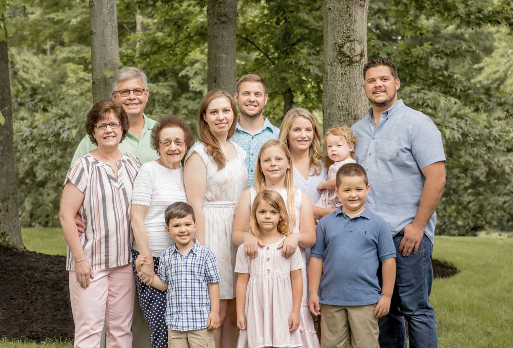Large multigenerational family posing together outdoors with green trees in the background.