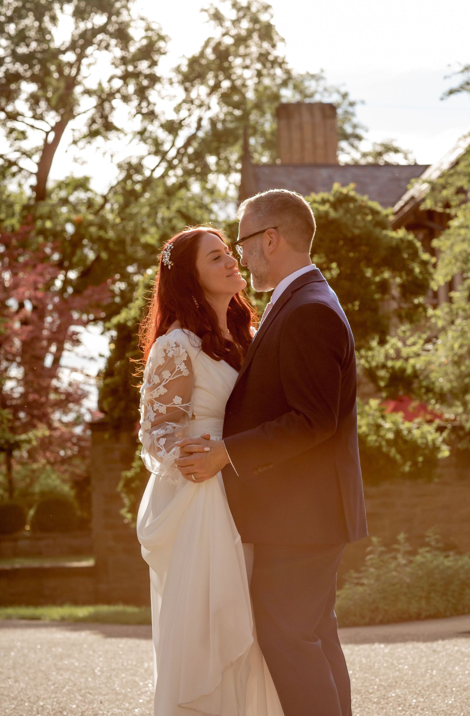 Bride and groom sharing tender moment in golden sunlight beside historic brick building.