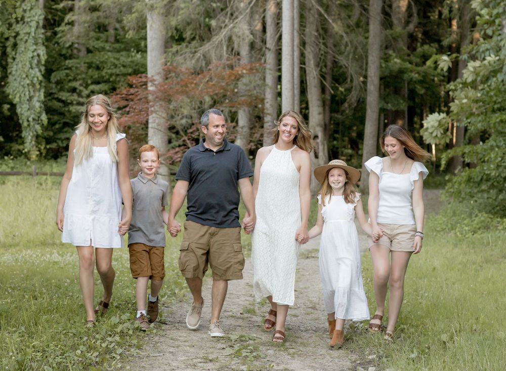 Happy family of six walking together on a forest path surrounded by tall green trees.