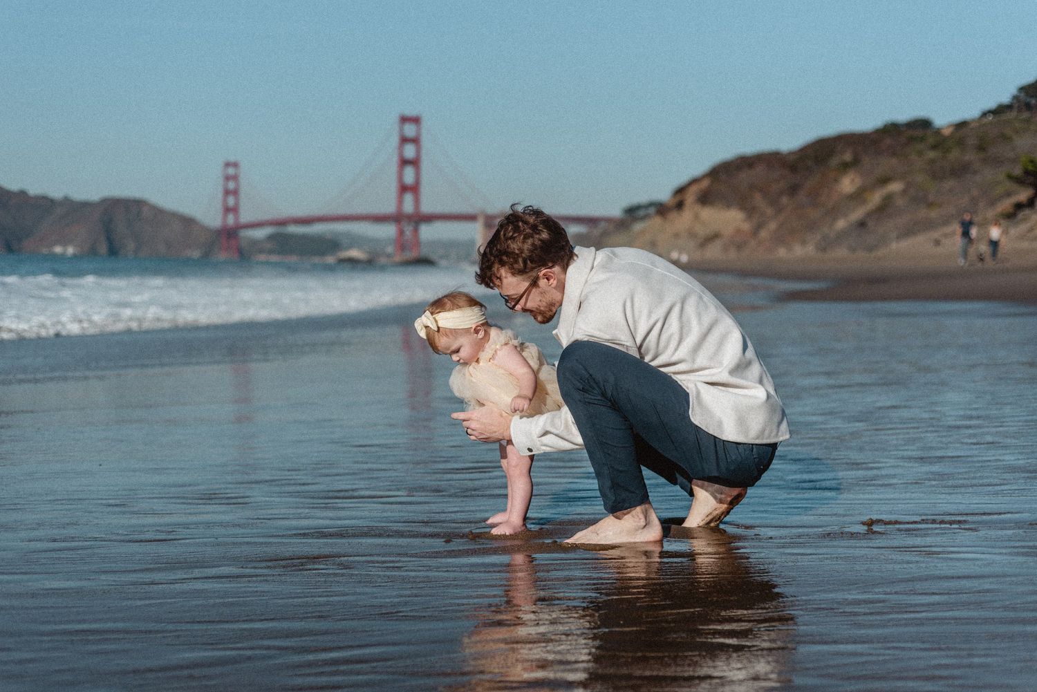 Parent and child playing in the waves at Baker Beach with the Golden Gate Bridge in the background.