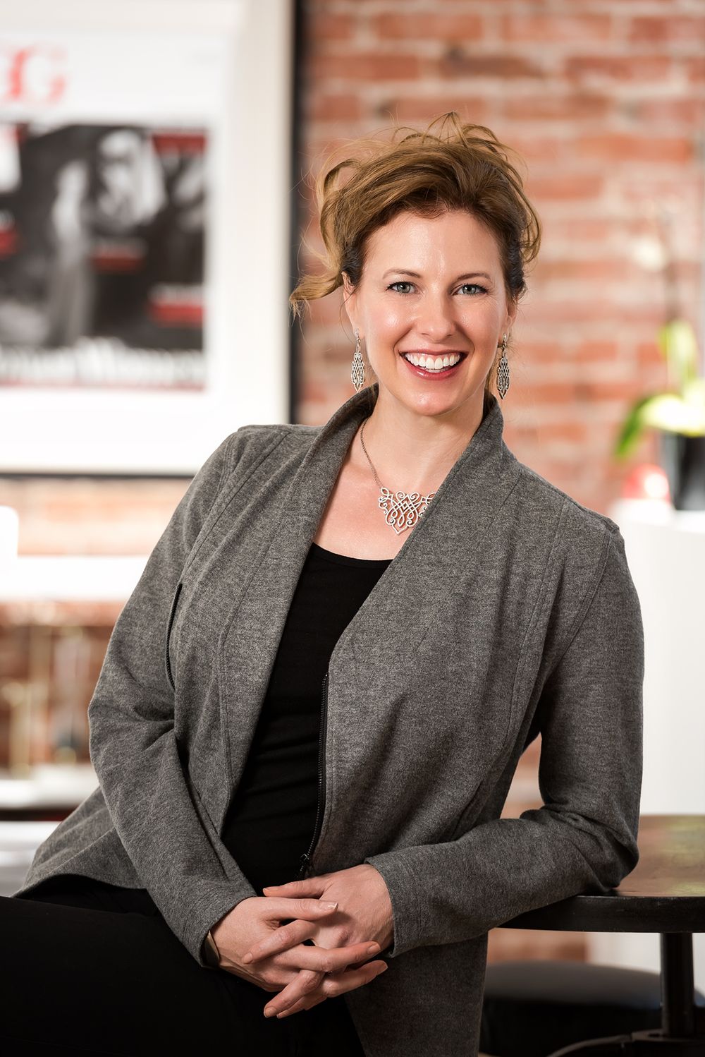 Professional portrait of woman in gray blazer seated in industrial office setting.