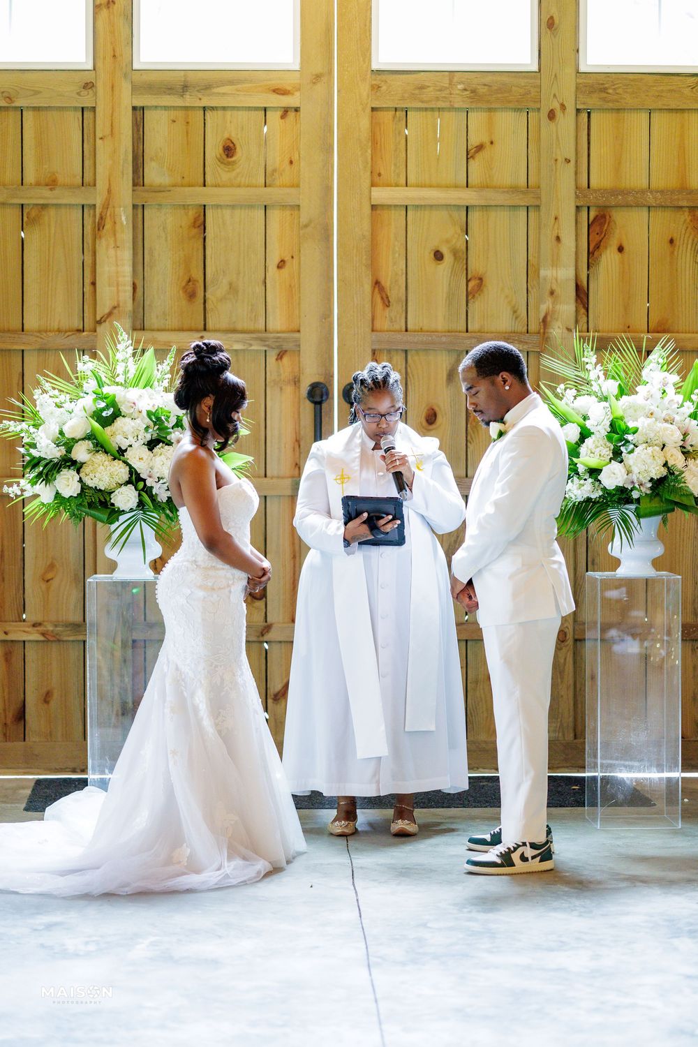 A wedding ceremony in progress with beautiful white floral arrangements flanking a wooden backdrop.