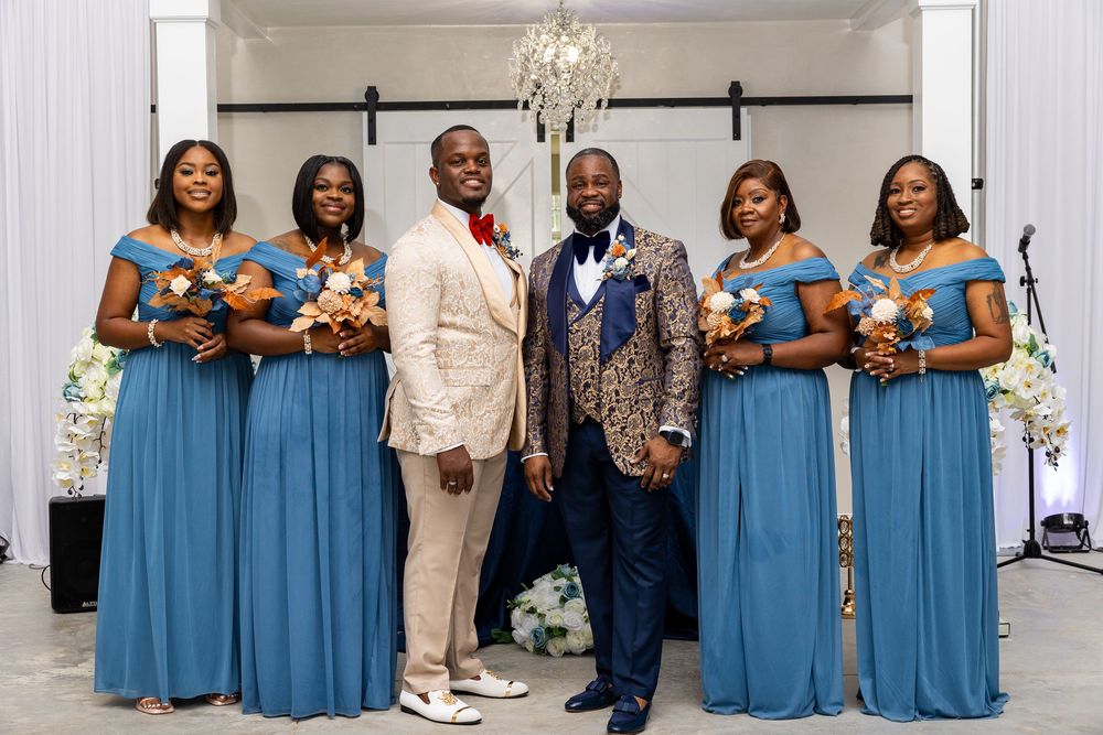Wedding party members pose together in coordinating blue dresses and formal attire at an elegant indoor venue.