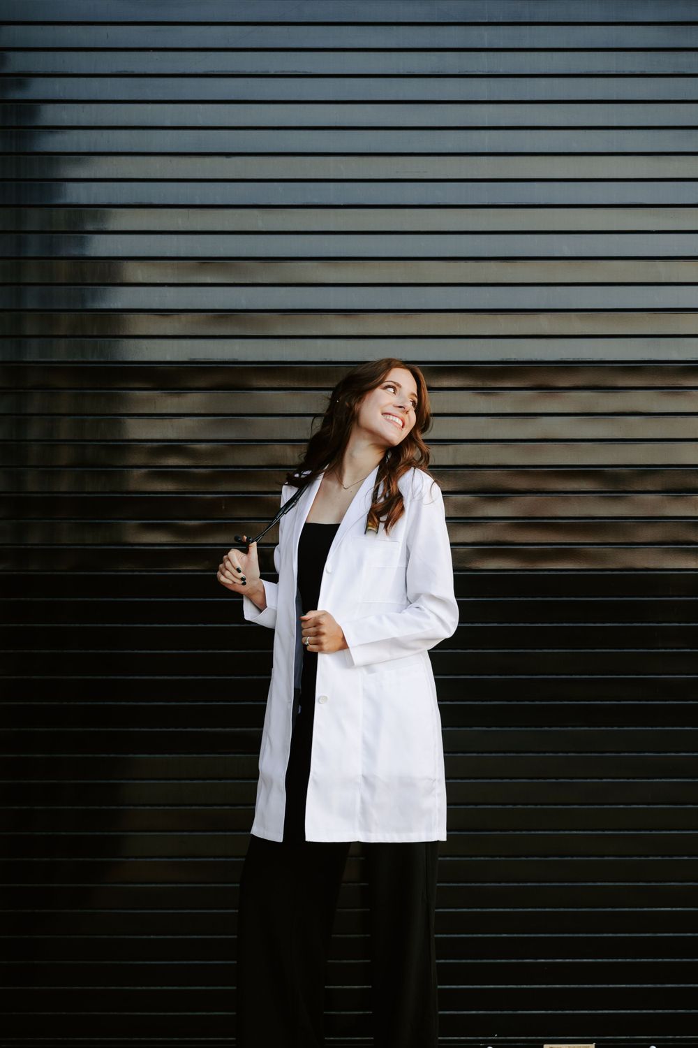 Person in white lab coat laughing against dark striped wall background.