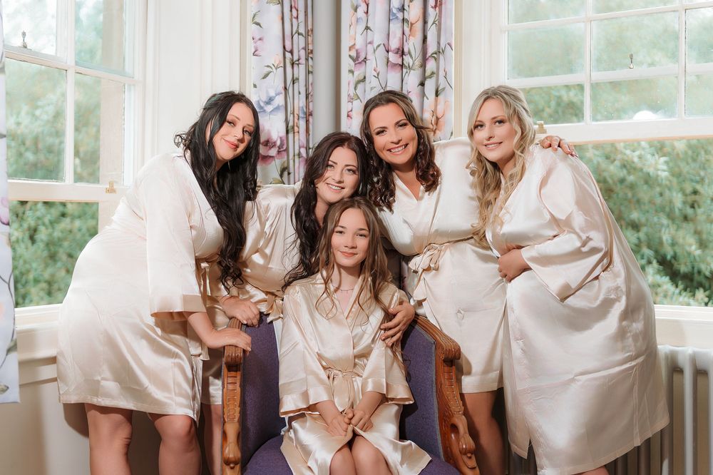 A group wearing matching cream-colored robes lounges together on a white couch in a sunlit room with floral curtains.