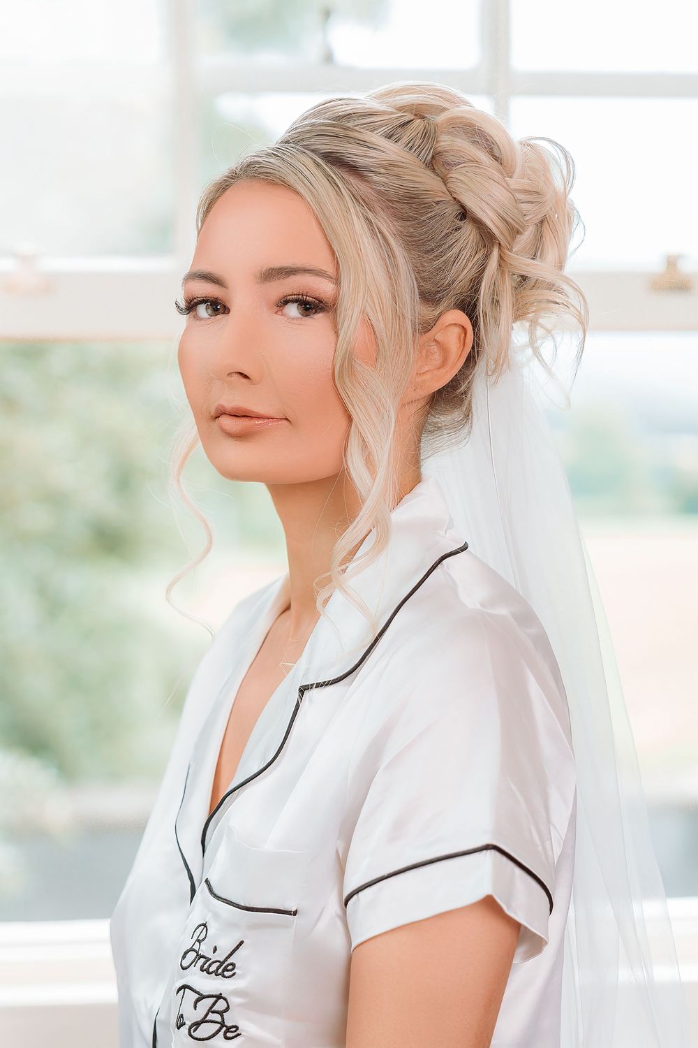 A woman in a white button-up shirt with black piping poses against a bright window background.