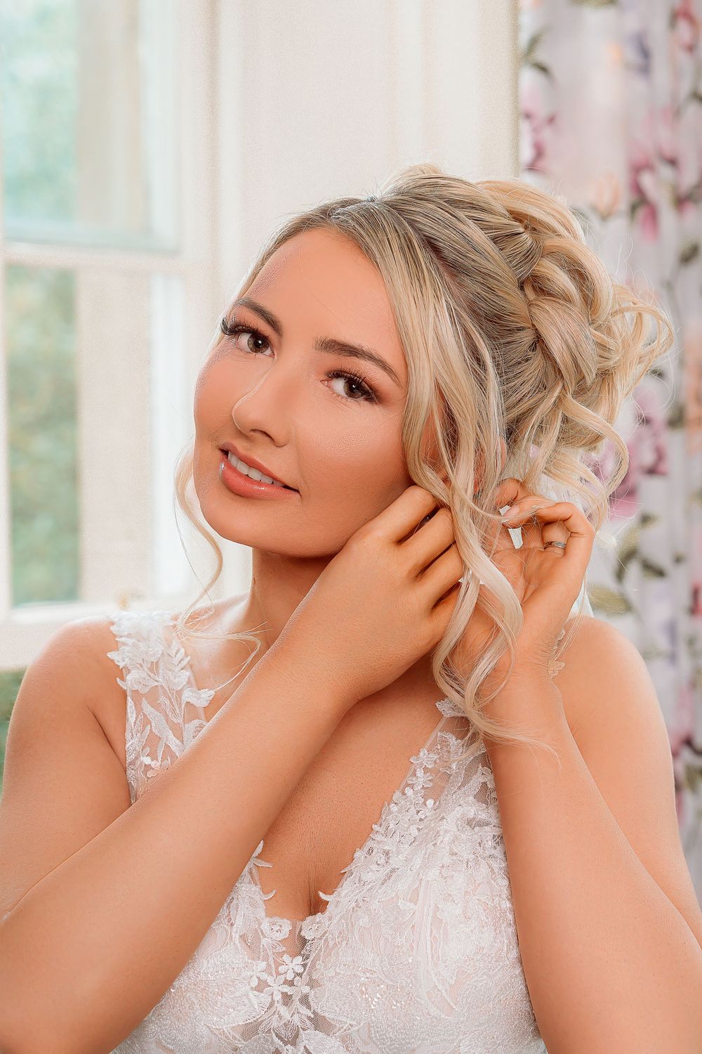 A bride in a delicate white lace wedding dress poses gracefully in a naturally lit setting.