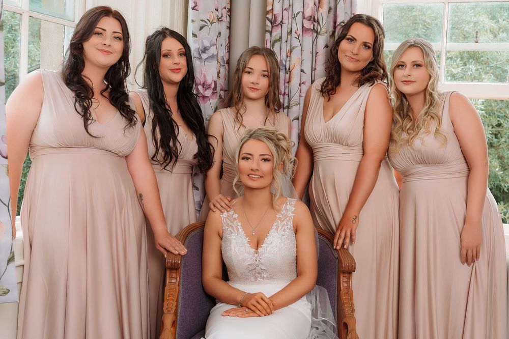 A group of bridesmaids wearing matching champagne-colored dresses pose together at a wedding celebration.