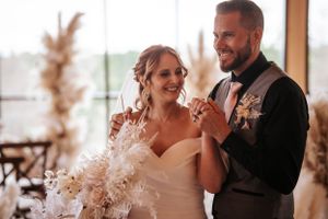 A romantic moment between newlyweds sharing their first dance in an elegant venue with pampas grass decor.