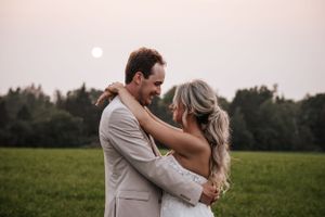 A romantic sunset embrace between newlyweds in a serene meadow with the moon rising.
