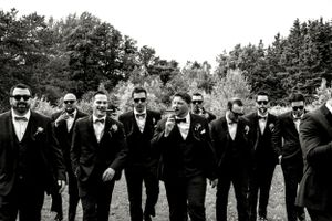 Groomsmen in black suits and sunglasses pose for a monochrome group photo.