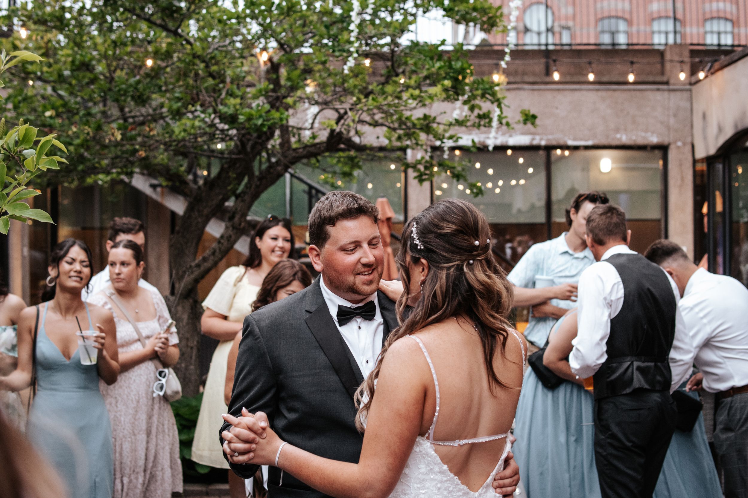Wedding guests dance and celebrate at an outdoor reception under string lights.