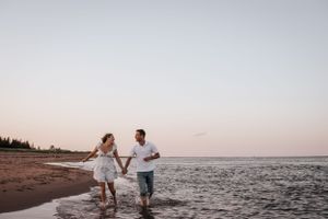 Couple splashing and walking hand in hand along a beach at sunset. Photo at Charlottetown PE