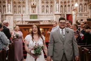 Happy couple walking down church aisle after ceremony surrounded by guests and ornate architecture.