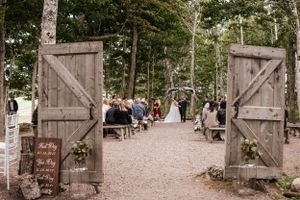 Rustic wooden barn doors frame outdoor wedding ceremony path with guest seating.