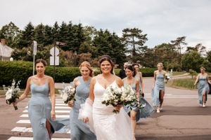 Wedding party walking along coastal path in coordinated light blue dresses.