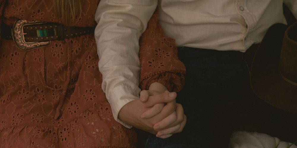 Close-up of a couple holding hands, woman wearing a brown eyelet skirt with turquoise belt.