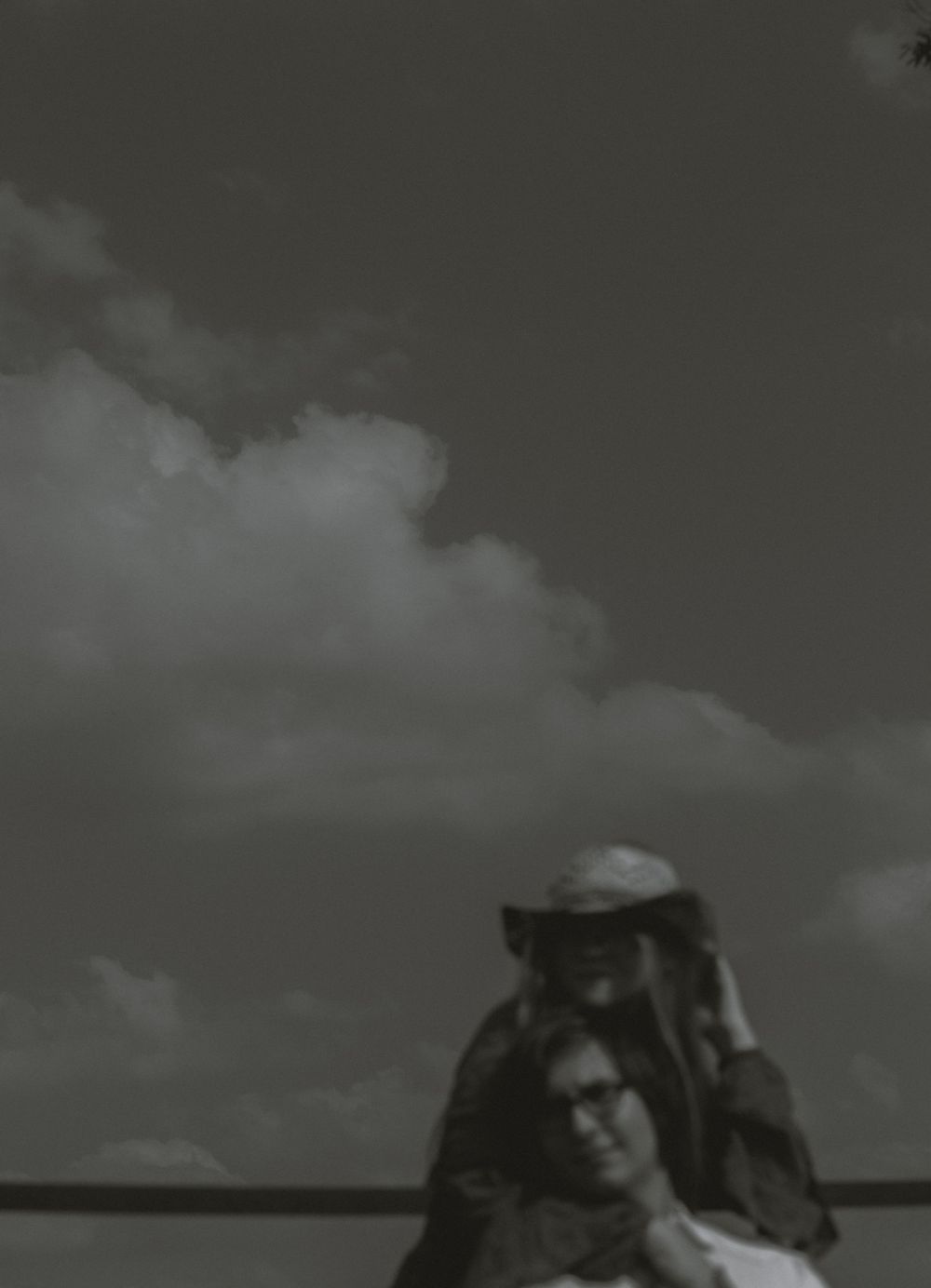 Black and white photo of a couple embracing under dramatic cloudy skies outdoors.