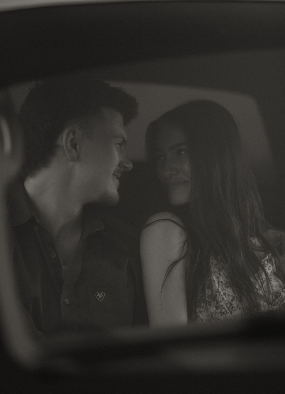Young couple sharing an intimate moment inside a car, captured in black and white photography.