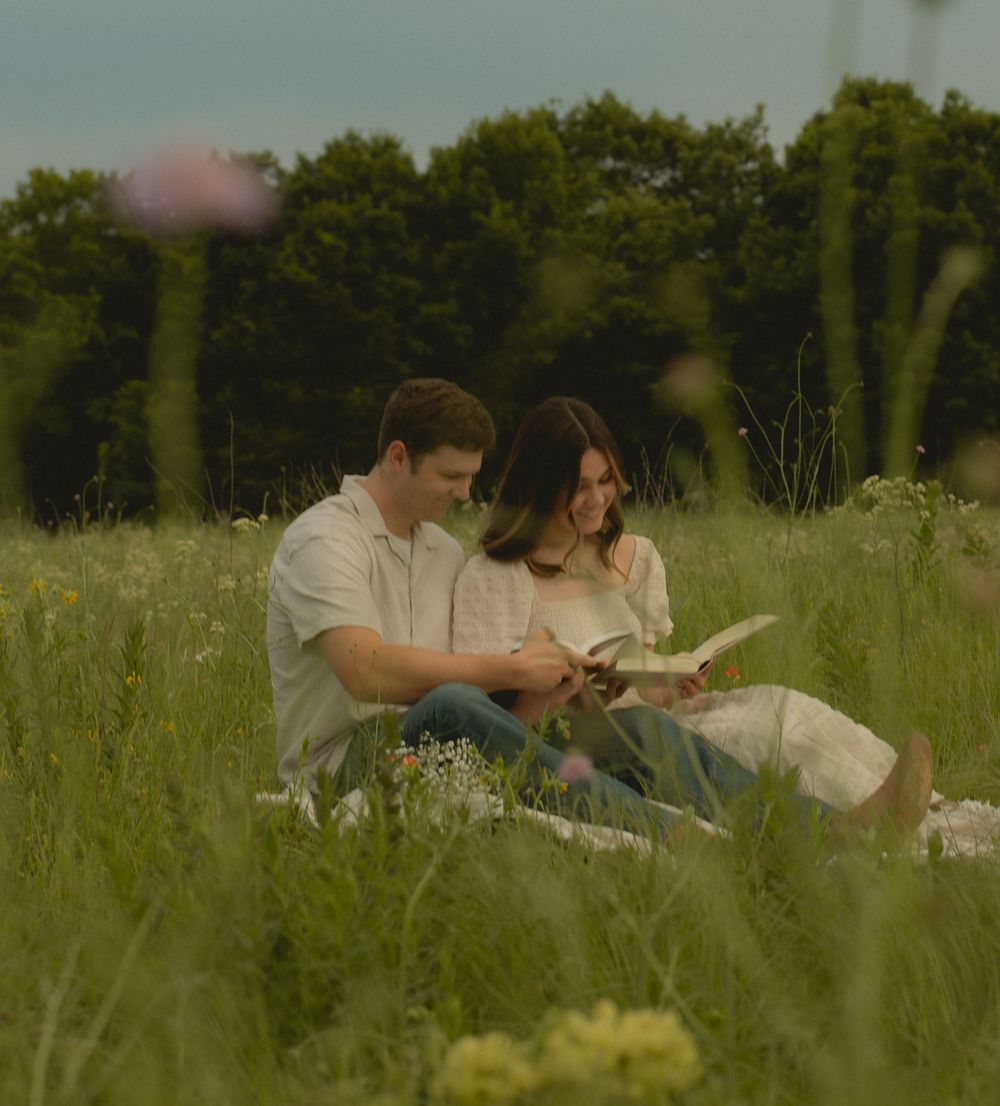 Couple sitting together in a wildflower meadow reading a book on a peaceful summer day.