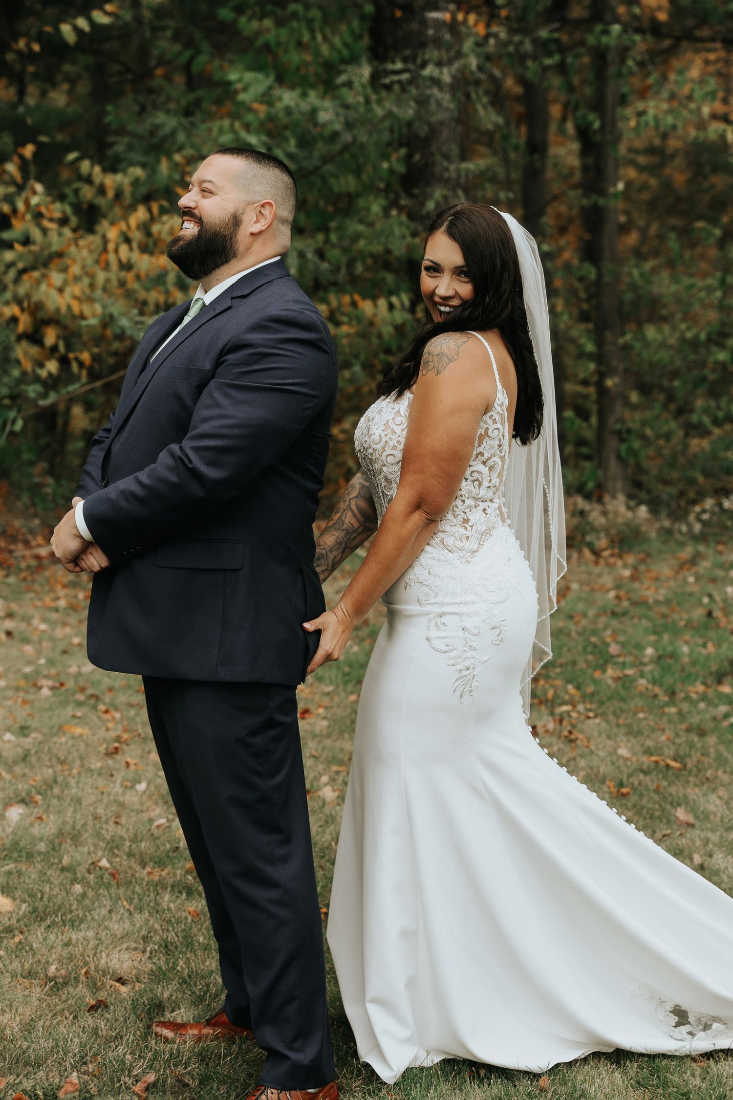 Wedding couple poses playfully outdoors during autumn with fallen leaves in the background.