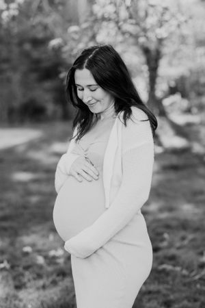 A peaceful maternity portrait of a woman in white dress standing outdoors.