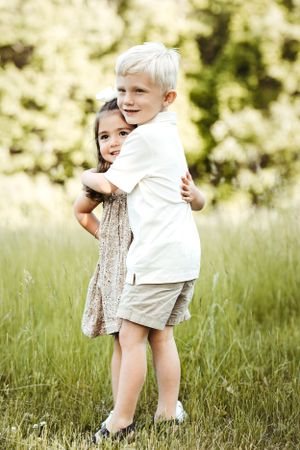 Two children share a playful hug while standing in tall grass.