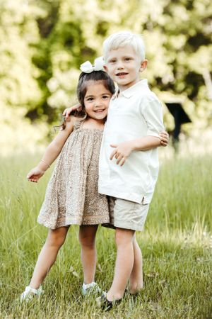 Two children pose together in coordinated outfits on a sunny day.