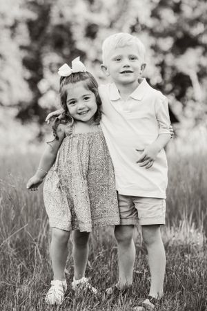 A black and white portrait of two children standing together in a field.