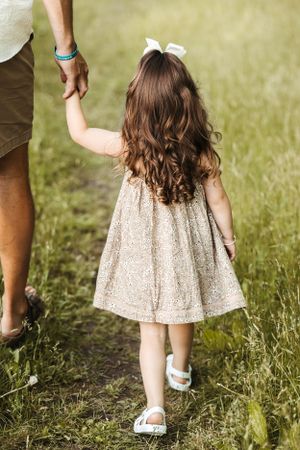 A child in a sparkly dress walks hand-in-hand through a grassy field.