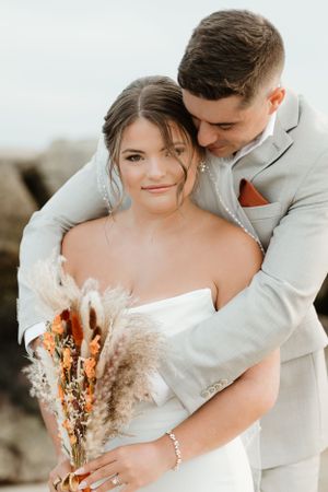 Romantic wedding portrait with couple embracing on rocky coastline.