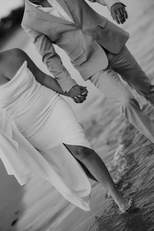Black and white photo of couple walking on beach in wedding attire.