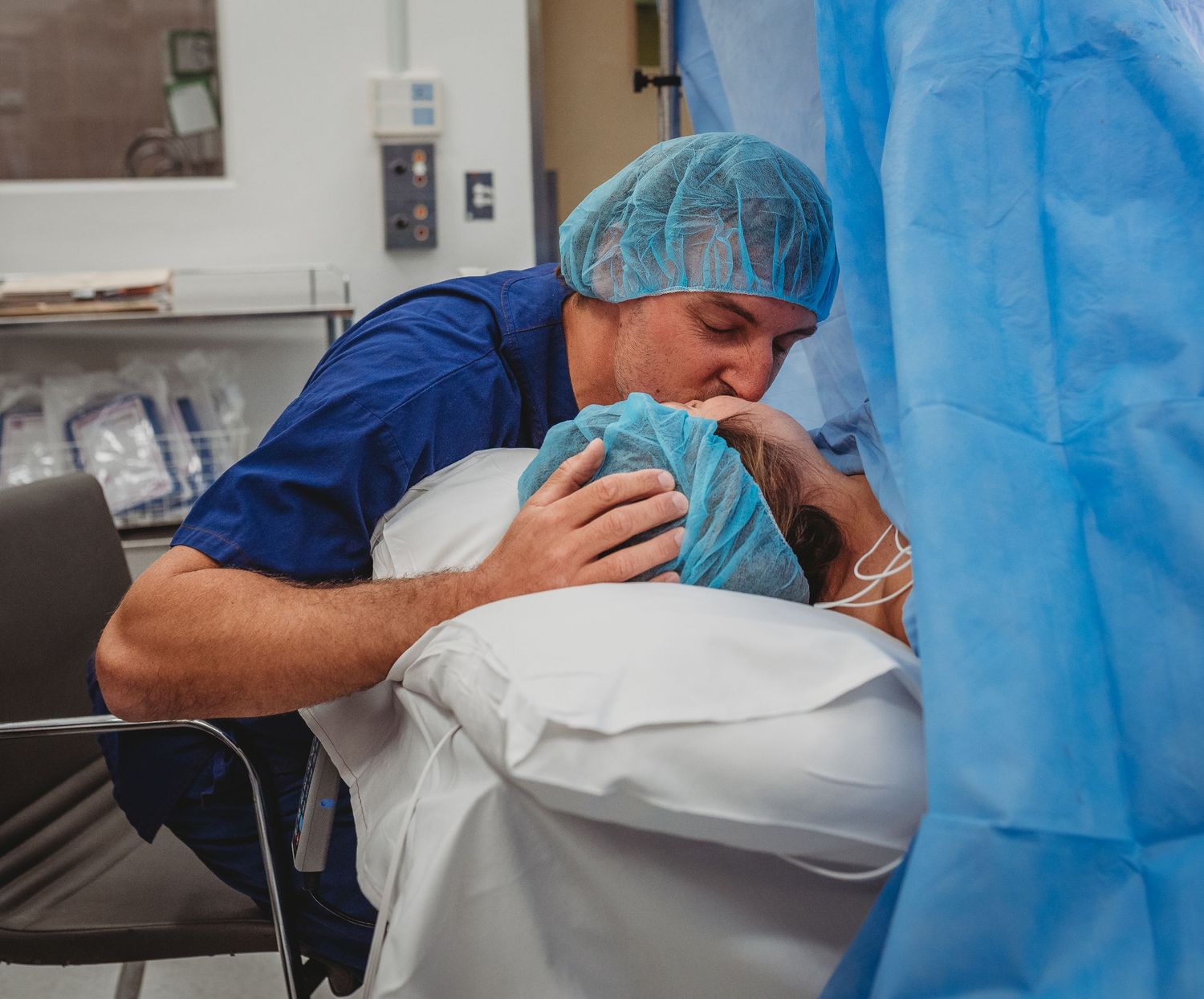 Medical team in blue scrubs and protective gear attending to patient during childbirth procedure.