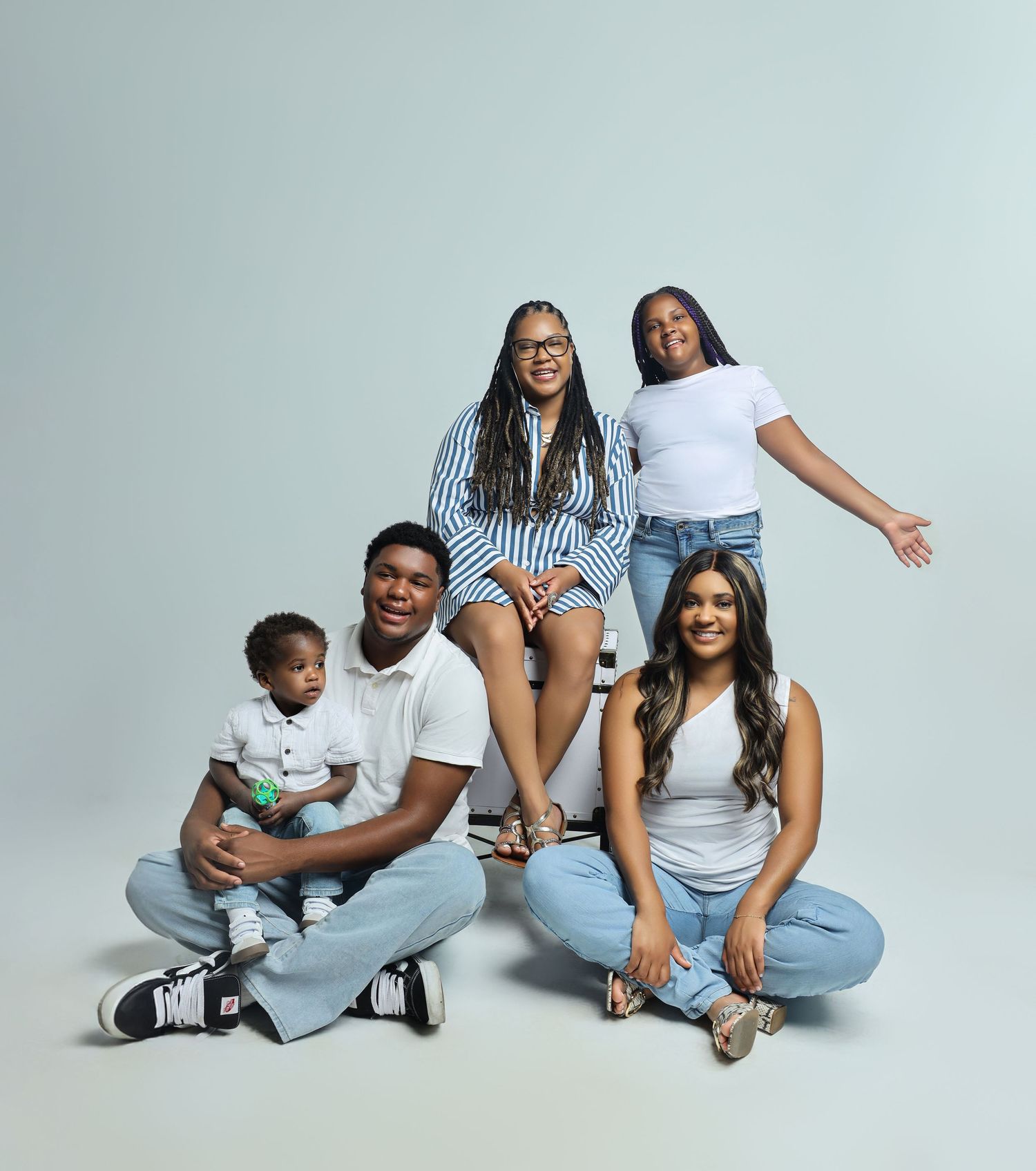 A happy and casual group poses together in a studio setting wearing jeans and simple tops against a light background.