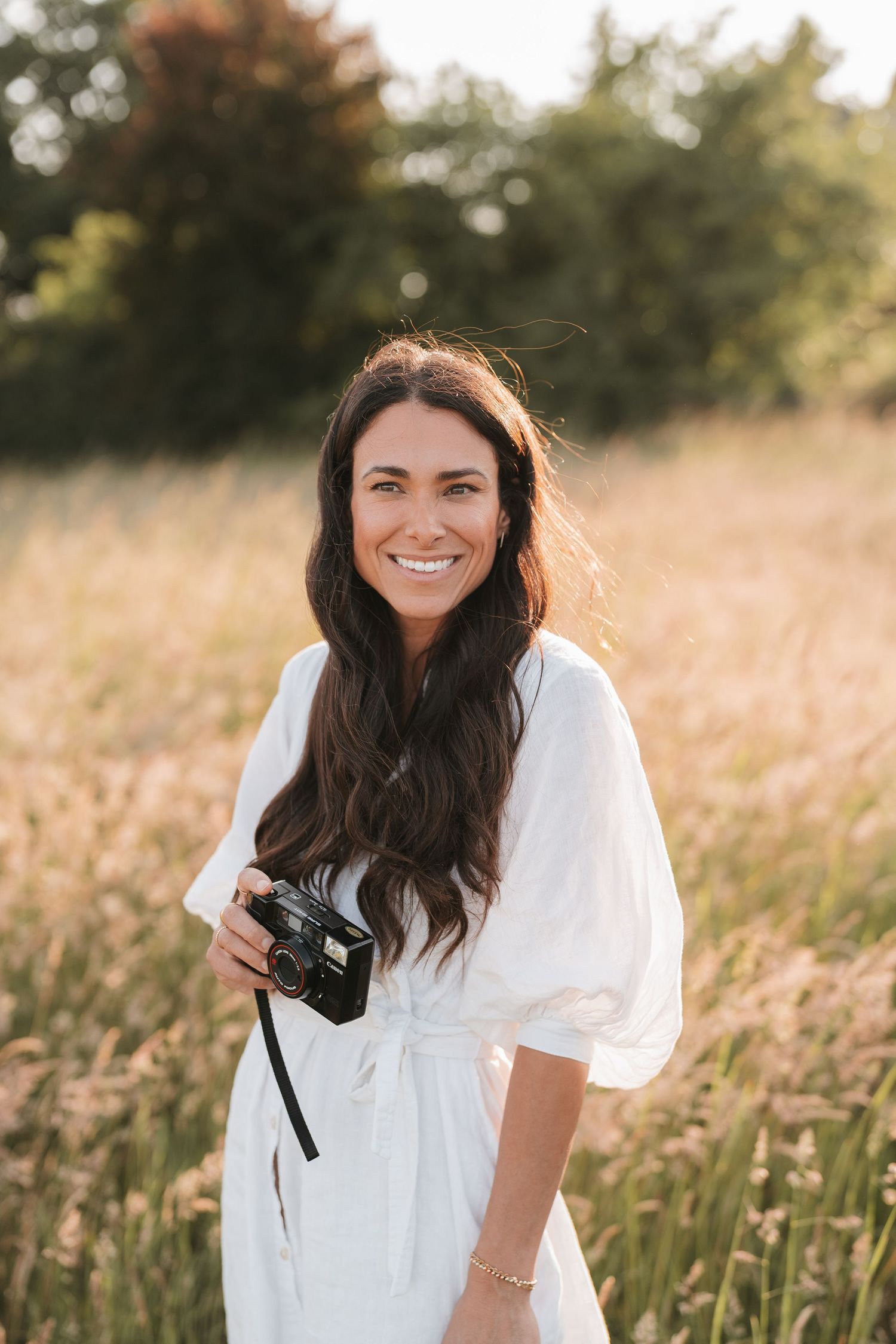 Photographer in white dress holding camera in golden summer field.