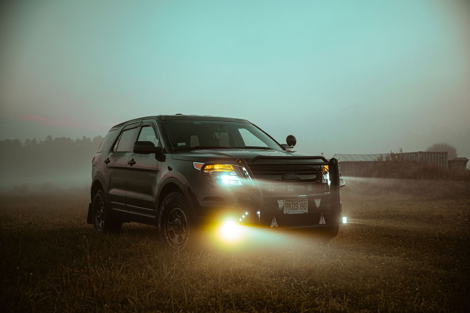 Black SUV with bright headlights photographed in foggy conditions at dusk.