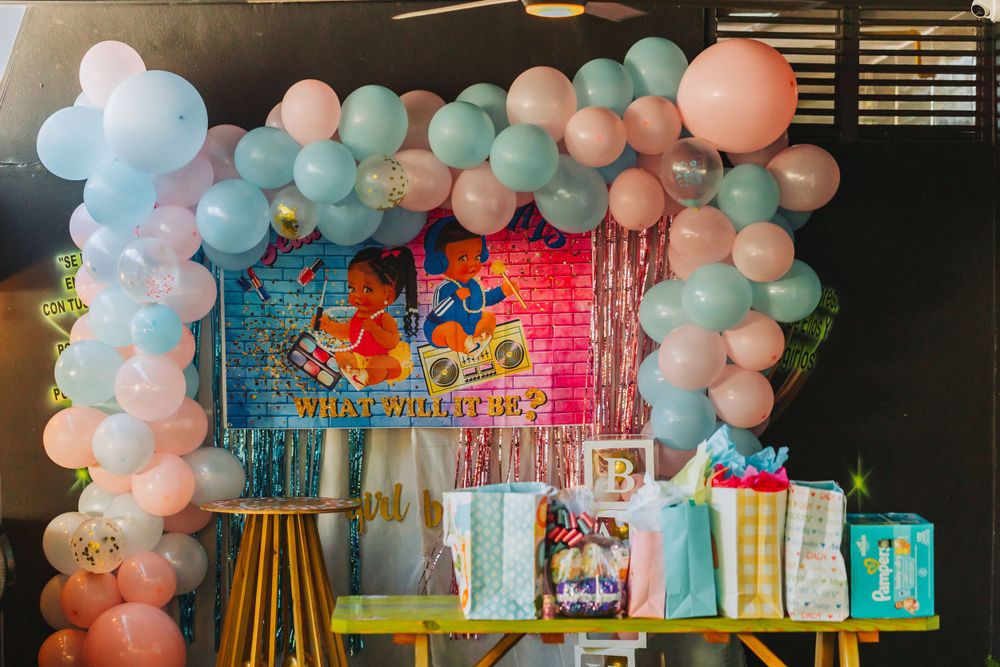 Baby shower decoration featuring pastel balloon arch and pink brick wall backdrop.