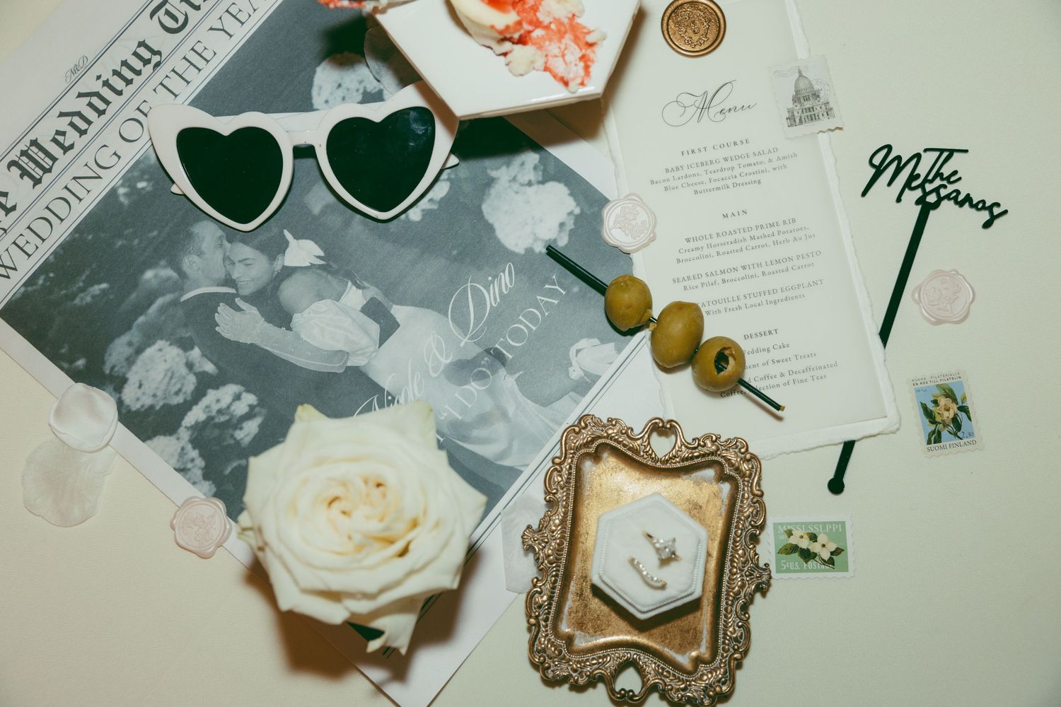 Wedding flatlay with heart sunglasses, vintage frame, and decorative elements.