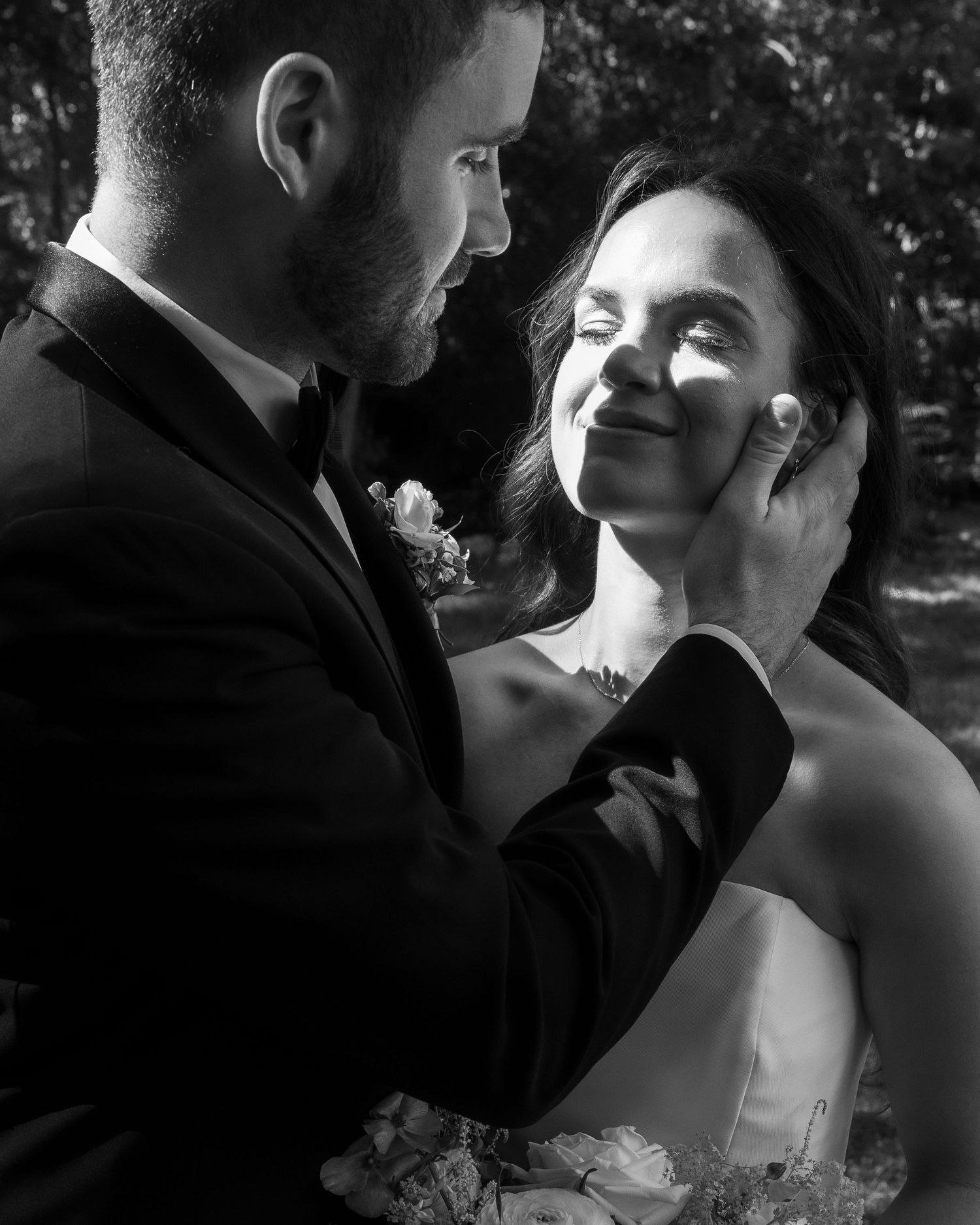 Groom tenderly cups brides face in romantic black and white wedding portrait outdoors.