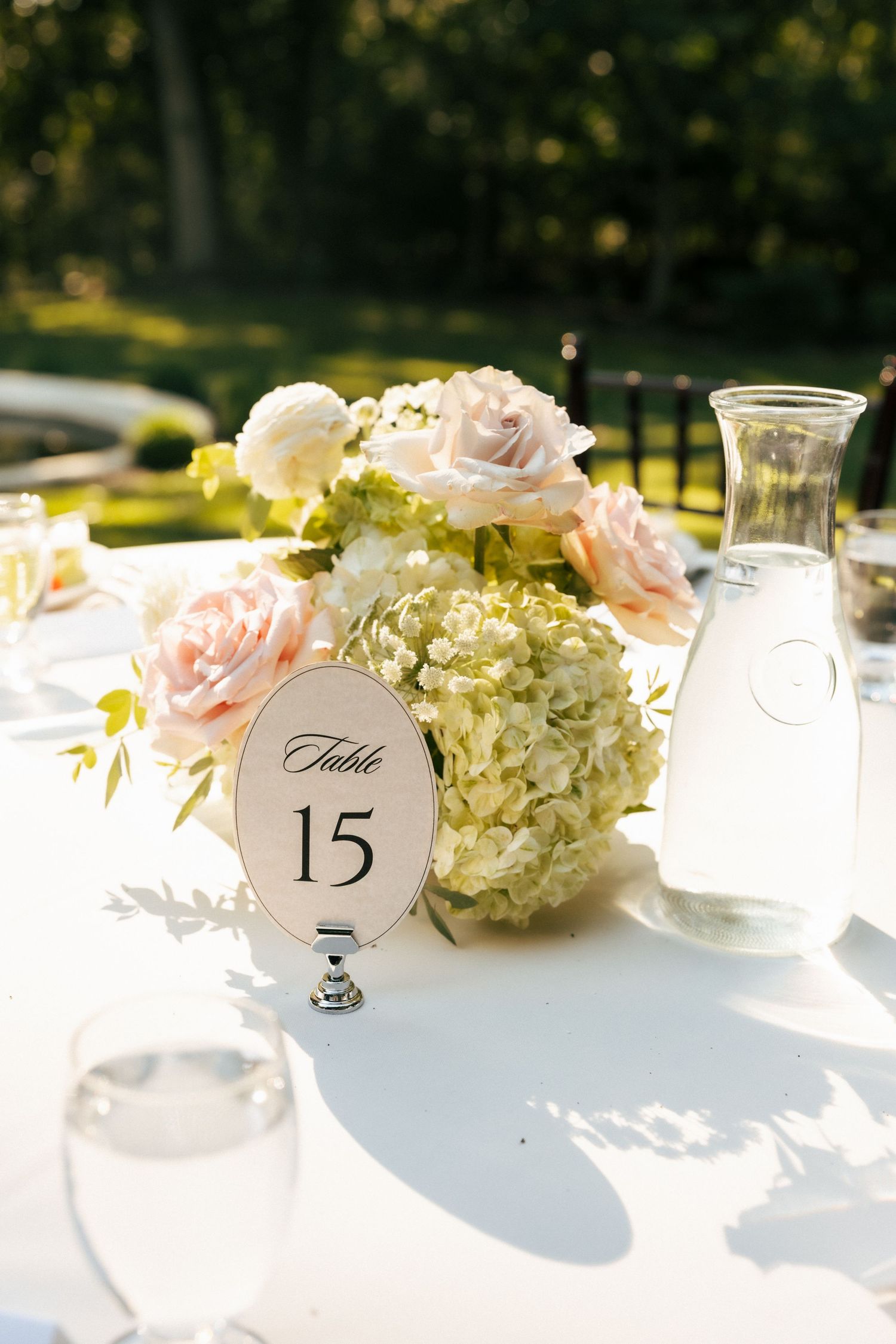 Elegant wedding table centerpiece with blush roses and hydrangeas beside a Table 15 sign.