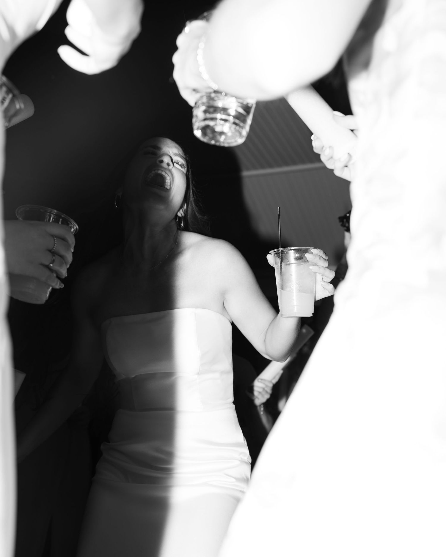Black and white photo of a bride in strapless gown laughing joyfully while holding a drink at a wedding reception.