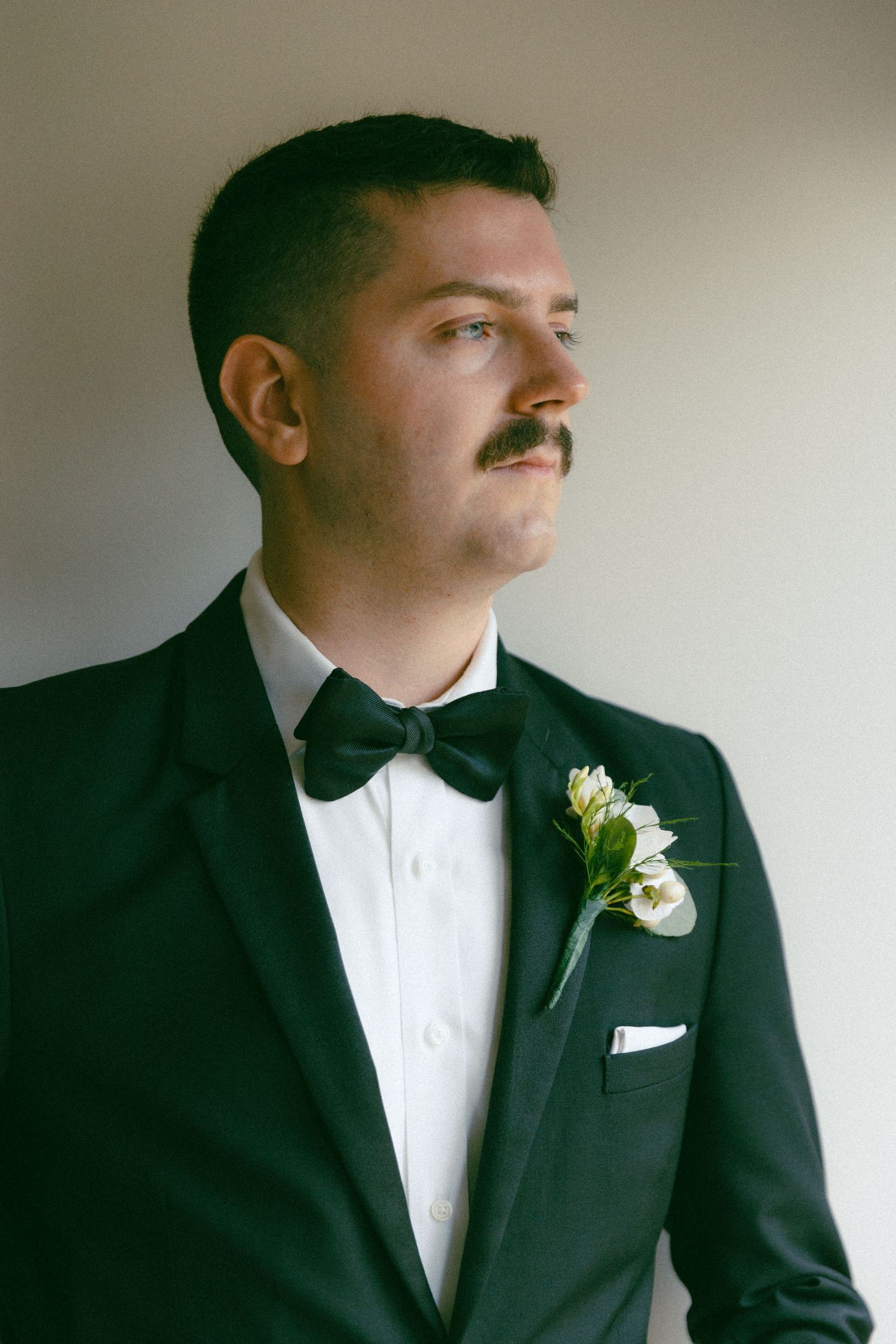 A groom in classic black tuxedo with white boutonniere and bowtie.