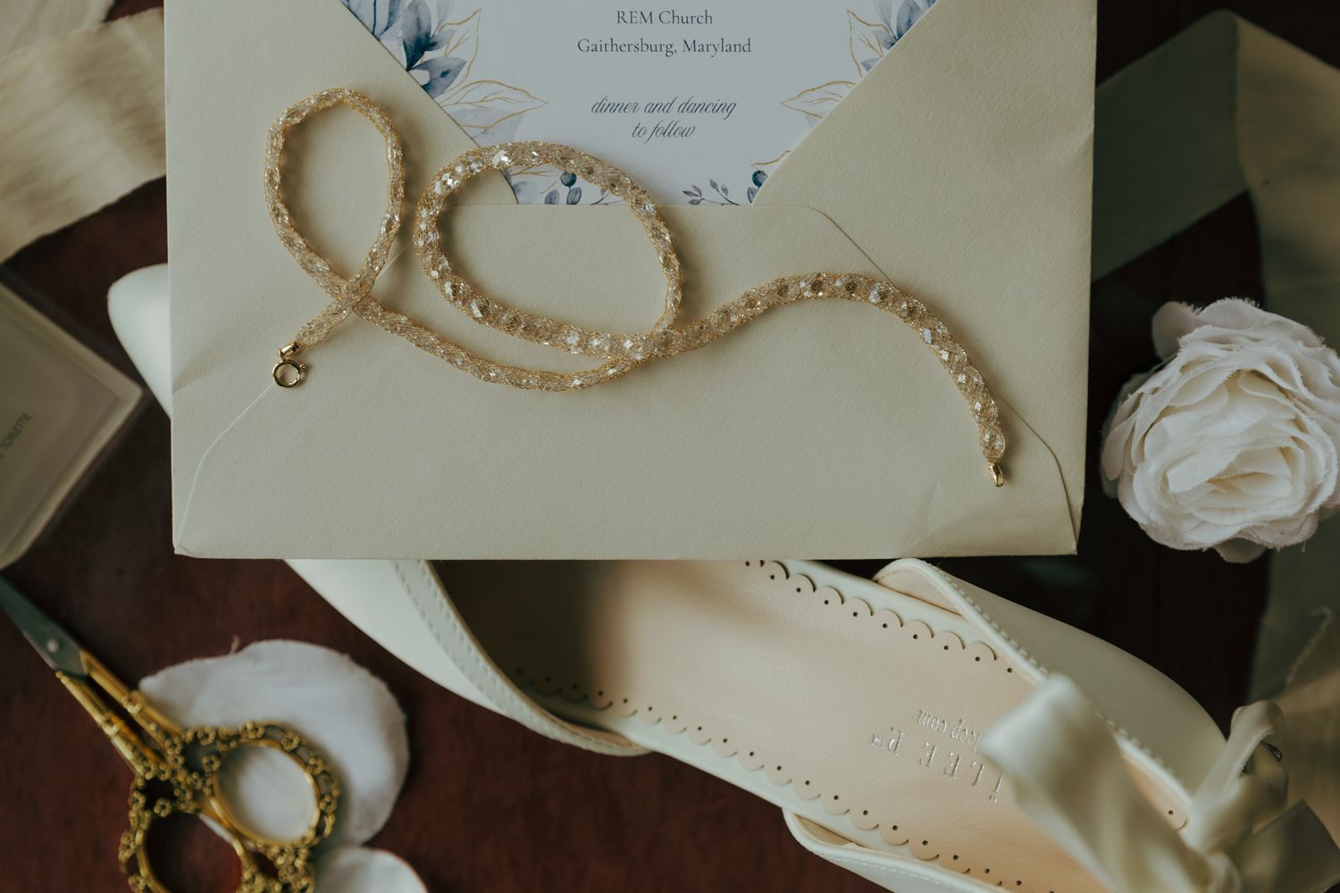 Wedding details flatlay with pearl necklace, invitation and white shoes.