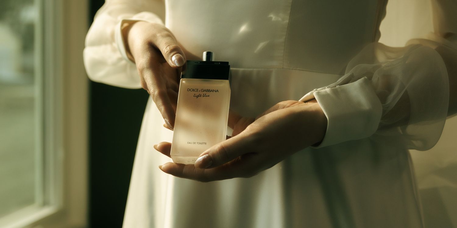 Hands holding an elegant perfume bottle in soft natural lighting.