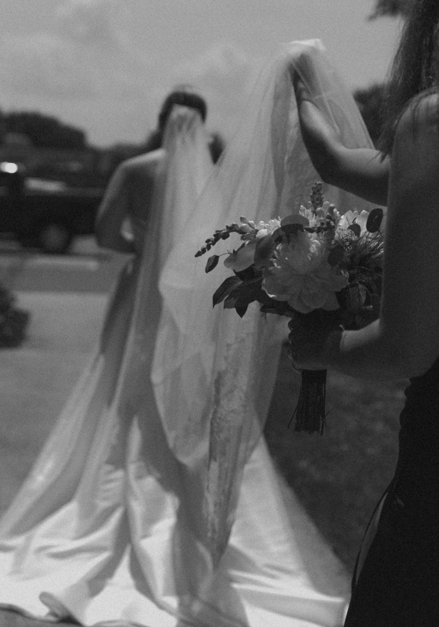 Black and white image of flowing wedding dress and veil with bouquet detail.