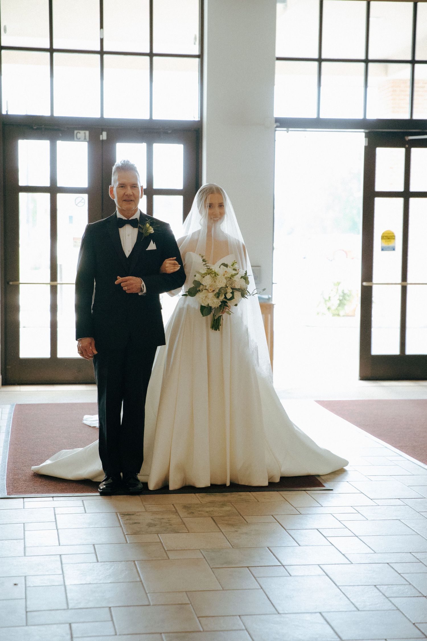 Wedding ceremony entrance with elegant hardwood floors and tall windows.