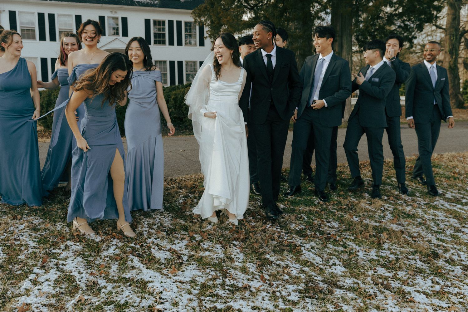 Wedding party in coordinated blue dresses and dark suits poses outdoors.
