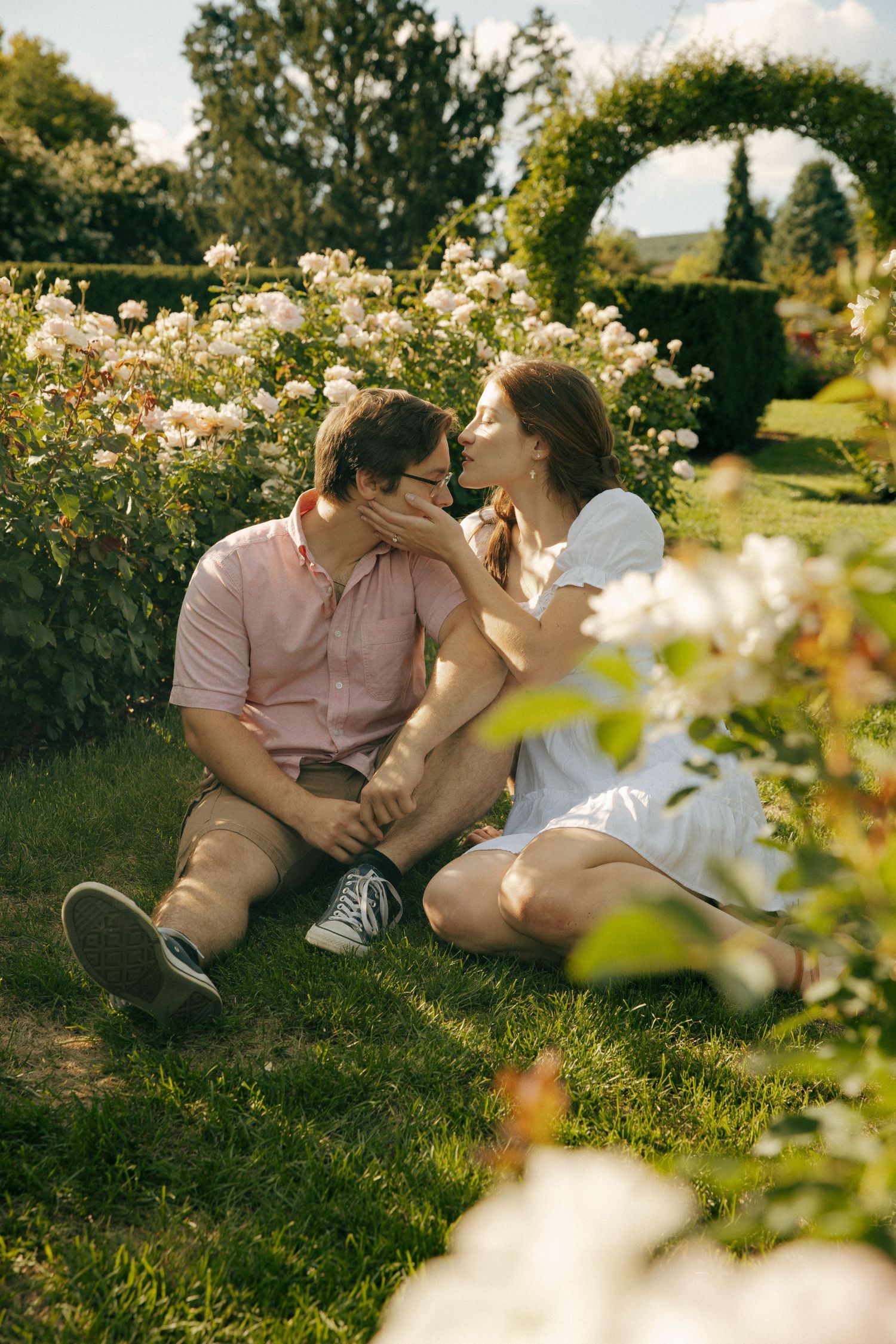 Romantic moment shared in a blooming rose garden with an arched trellis backdrop.