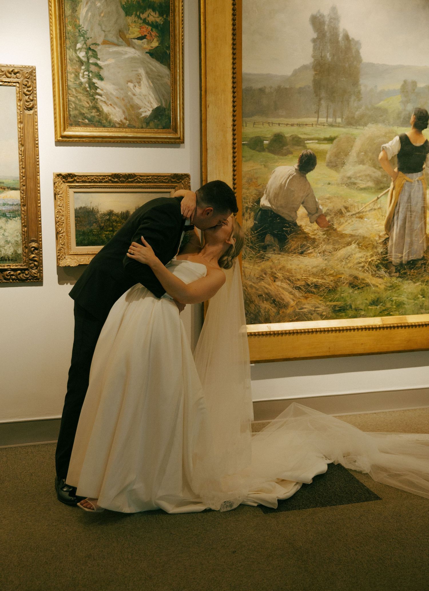 Romantic moment between newlyweds in art gallery with pastoral paintings in background.